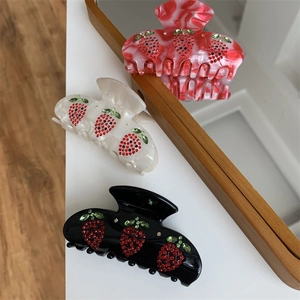 Dettaglio di fermagli per capelli a fragola in nero, crema e marmo con strass rossi