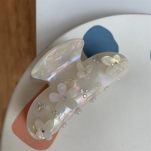 Dettaglio di molletta per capelli perlata con fiori bianchi, farfalle e strass colorati