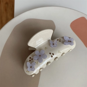 Dettaglio macro di un fermaglio per capelli crema con fiori viola, farfalle e strass