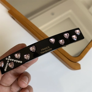 Close-up of black hair clip with pink rhinestone hearts and handmade gold lettering