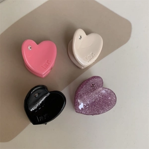 Detail of four mini heart-shaped resin hair clips with rhinestones and engraved logo