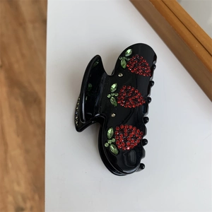 Dettaglio della molletta per capelli nera con decorazioni in strass a forma di fragola