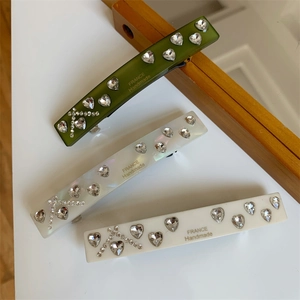 Close-up of rectangular resin hair clips with crystal heart and diamond letter K details