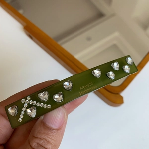 Detail view of handmade dark green hair clip featuring heart rhinestones and an A-letter design