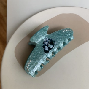 Macro detail of a light blue marble-textured hair claw with cat motif and tiny rhinestones