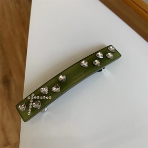 Detailed view of olive green acetate hair clip with crystal hearts and gold engraving