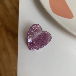 Detail of a purple heart-shaped hair claw clip with sparkling glitter and a pink crystal