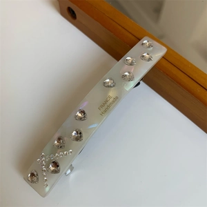 Detail of white acetate hair clip featuring crystal hearts and France Handmade text