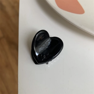 Close-up of a small black heart-shaped hair claw clip with glossy resin finish and mini text