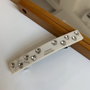 Close-up of heart-shaped rhinestones and letter R engraving on ivory white hair clip