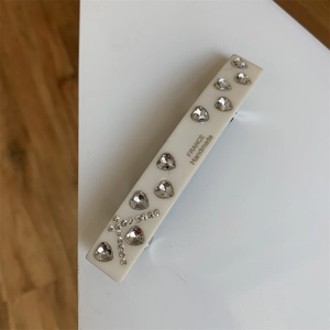 Macro shot of white handmade hair clip with heart-shaped crystals and round diamonds