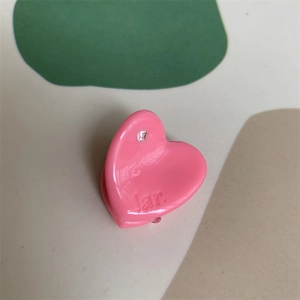 Close-up of pink heart hair clip with rhinestone and lar. lettering on soft background