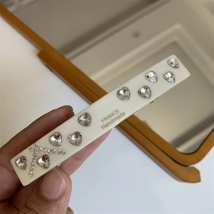Macro detail of cream hair clip with heart rhinestones and France Handmade logo