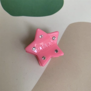 Detail view of mini pink star-shaped hair claw with engraved text and sparkly rhinestones