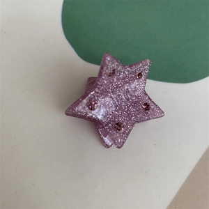 Macro detail of star-shaped hair claw clip in purple glitter with inlaid pink rhinestones