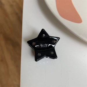 Macro view of a small black star-shaped hair claw clip with rhinestones and star engraving