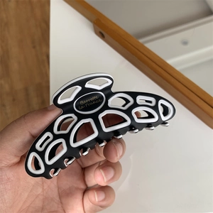 Close-up of a black and white geometric hair claw clip with golden French lettering detail