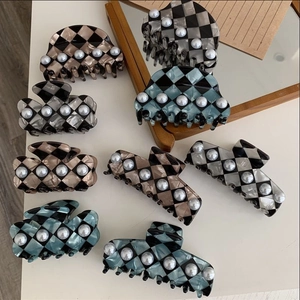 Detail view of checkered pattern hair claws with pearl accents in various colors on white desk