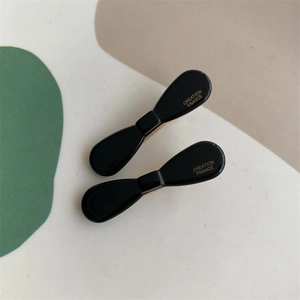 Detail of two black acetate bow hair clips with gold Creation France lettering