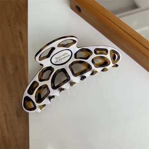 Detail shot of white and tortoiseshell resin hair claw clip with oval logo branding