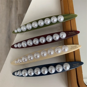 Close-up of four colored French barrettes with white pearls and elegant gold lettering