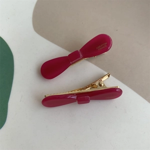 Detail of rose pink acetate bow hair clips with gold metal duckbill clamps and engraved text