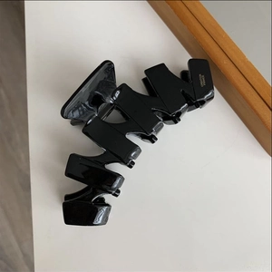 Detailed close-up of a glossy black acetate hair claw clip with French geometric design