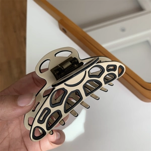 Close-up of a stylish hollow-out cream and black resin hair claw with metal spring