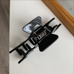 Detail of a large black glossy hair claw clip featuring a metallic spring and polished finish