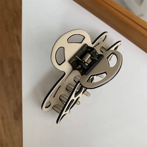 Detail view of a minimalist cream hair claw clip with black edges and metal spring mechanism