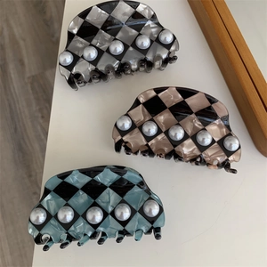 Three checkerboard pearl hair claws in black, brown, and blue colors set on white stand