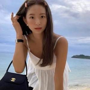 Classic small black flap handbag with golden oval logo emblem shown in outdoor beach setting