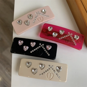 Detail of four acrylic heart rhinestone hair clips in pink, black, and cream colors