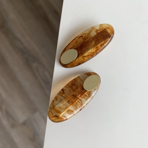 Detail showing a pair of tortoise shell oval hair clips with gold metal plates on a white desk