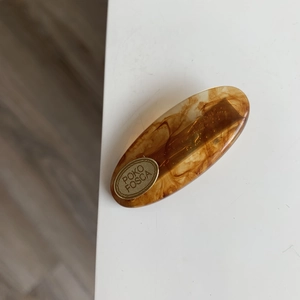 Detail view of oval tortoiseshell resin hair clip with golden POKO FOSCA metal logo plate