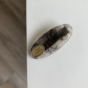 Detailed macro view of an oval resin hair clip with smoky marble texture and gold lettering