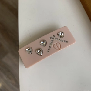 Detail showing pink resin hair clip with crystal hearts and engraved logo texture