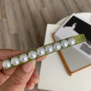 Detail view of olive green resin barrette with elegant pearls and steel engraved logo