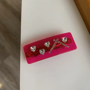 Detail of pink acrylic hair clip featuring sparkling heart rhinestones and a cross pattern