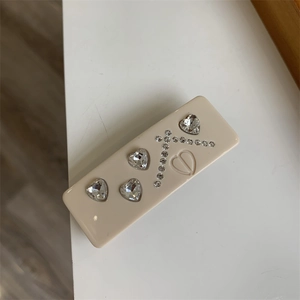 Detail of a beige hair clip with heart-shaped rhinestones and luxury CD logo engraving
