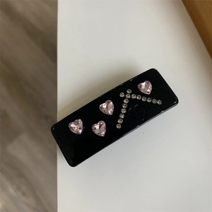 Detail of black rectangular hair clip with pink heart rhinestones and CD logo