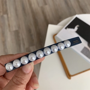 Detailed view of long navy hair clip with ten white pearls and gold La France lettering