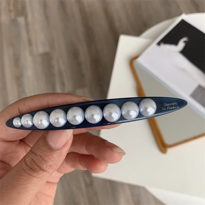 Detailed close-up of blue geometric hair clip featuring gradient pearls and gold lettering