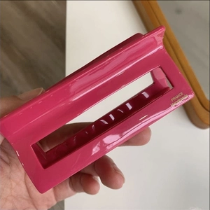 Detail of glossy red rectangular hair claw clip with golden handmade branding lettering