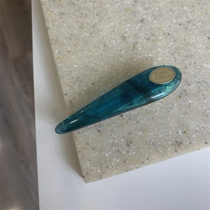 Close-up of translucent teal waterdrop hair clip with glossy finish on marble texture