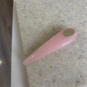 Detailed close-up of a pink glossy resin hair clip with a gold logo on a stone surface