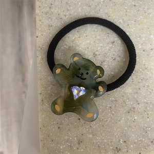 Detailed macro view of a green resin cartoon bear hair tie with colorful heart rhinestone