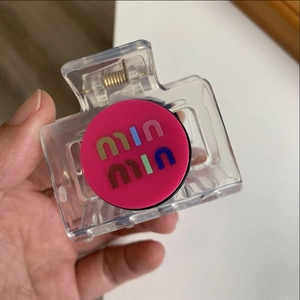 Detail of transparent hair claw clip featuring a pink disc with colorful brand logo