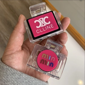 Close-up of square pink and clear hair claws with branded logo patterns held in hand