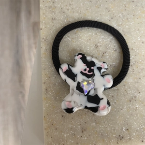 Close-up of black elastic hair tie with cow print bear charm and heart gemstone